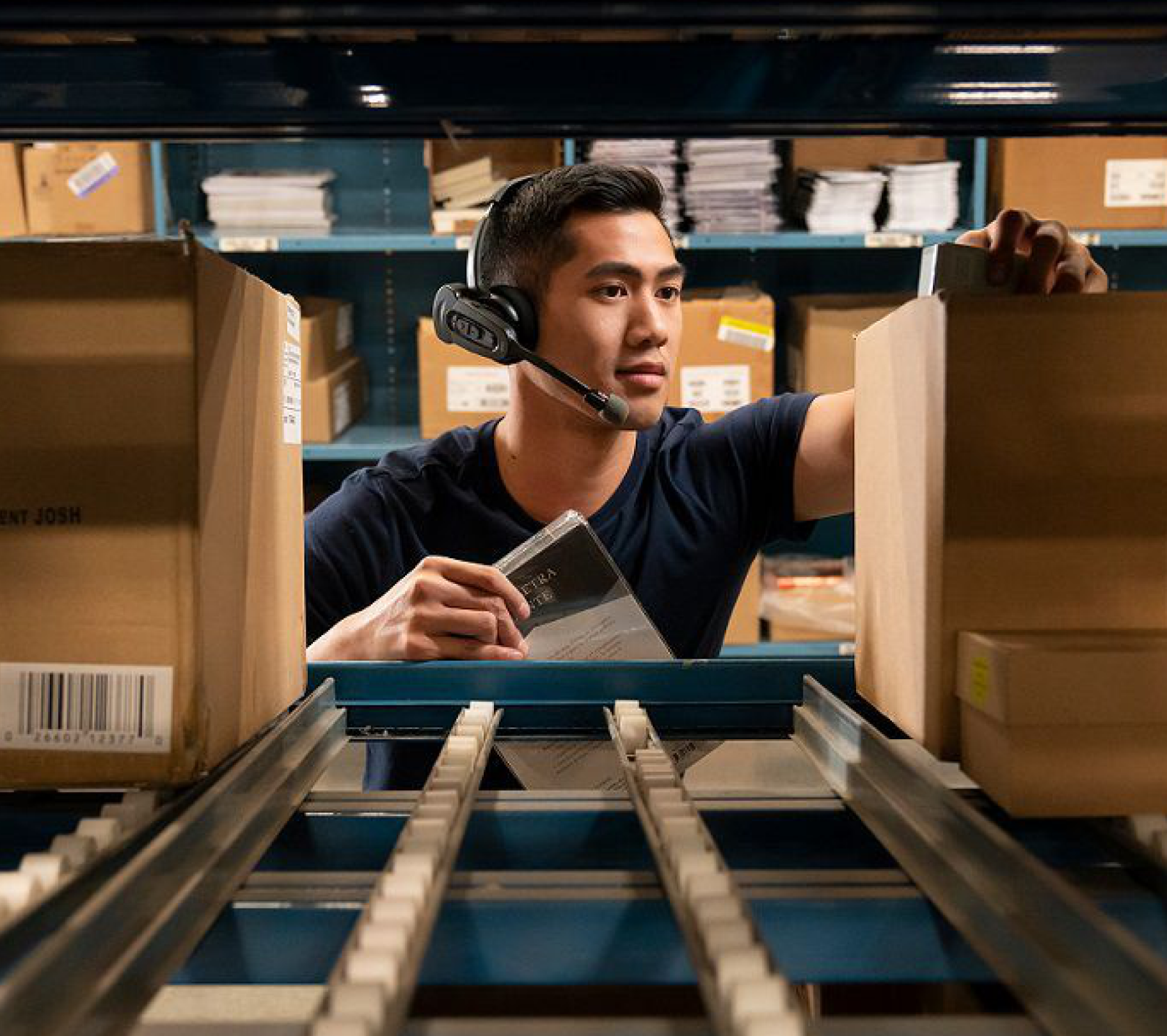 Warehouse employee using voice-picking headset while picking items from a conveyor rack.